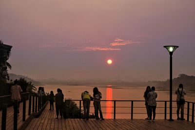 People by sea against sky during sunset