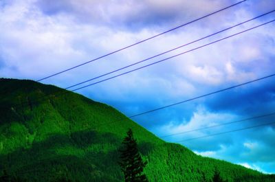 Low angle view of electricity pylon against cloudy sky