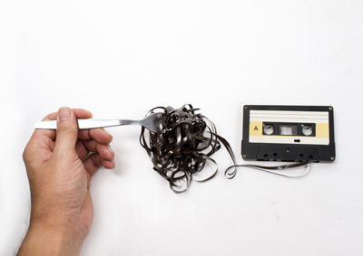 Cropped hand of man holding tangled reel with fork by cassette on white background