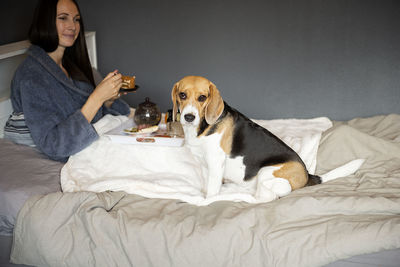 Smiling woman with dog sitting on bed at home
