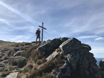 Low section of man standing by cross on mountain against sky