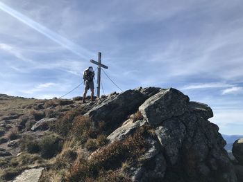 Rear view of man standing by religious cross on rock against sky