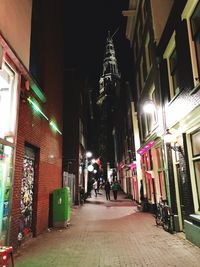 People walking on illuminated street amidst buildings at night