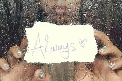 Close-up of woman holding text message on paper seen from wet glass