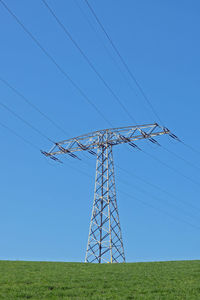 Low angle view of electricity pylon on field against clear sky