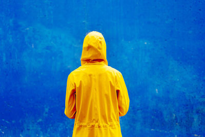 Rear view of person wearing raincoat against blue wall