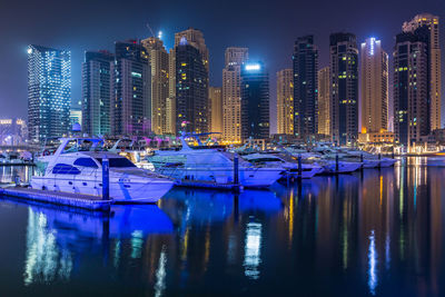 Boats moored in canal by illuminated buildings in city at night