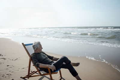 Senior man sitting on chair by seashore at beach