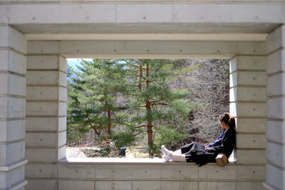 Side view of woman sitting by window