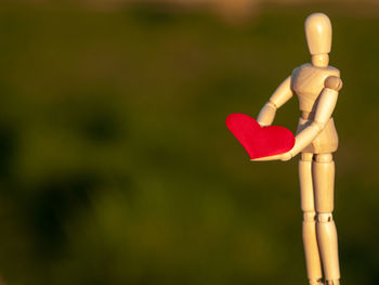 Close-up of wooden figurine holding red heart shape outdoors