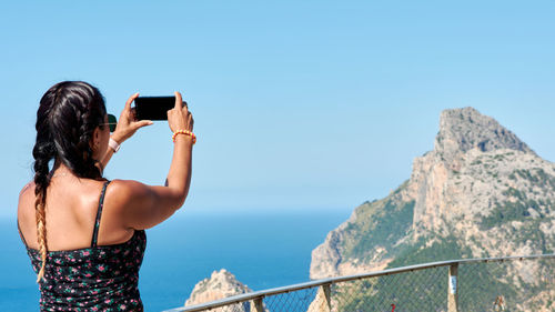 Rear view of woman photographing on mobile phone against sea