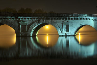 Illuminated arch bridge over river against sky during sunset