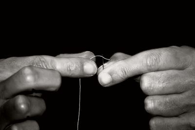 Cropped hands threading sewing needle against black background