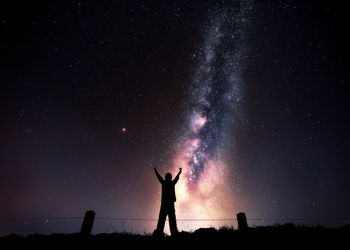 Low angle view silhouette of man standing with arms raised standing against sky at night