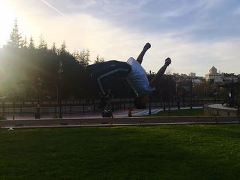 Man jumping in park against sky in city