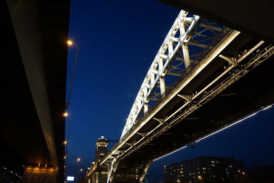 Low angle view of illuminated bridge and buildings against sky at night
