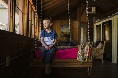 Thoughtful boy sitting on swing at home