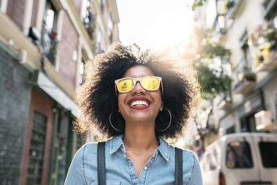 Smiling young woman wearing sunglasses against buildings in city