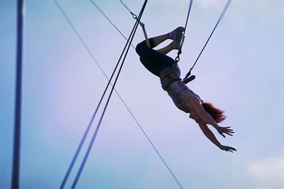 Low angle view of man hanging on rope against sky