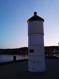 Lighthouse by lake against clear sky during sunset