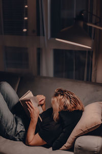 Woman reading book while leaning on sofa home