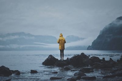 Rear view of man standing on rock by sea against sky