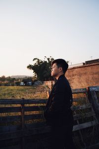 Side view of young man looking away against clear sky