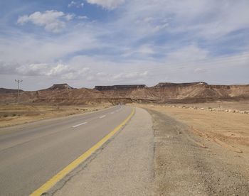 Road by desert against sky