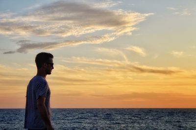 Man standing by sea against sky during sunset