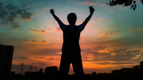 Silhouette man with arms outstretched standing against sky during sunset