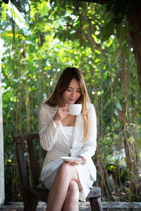 Businesswoman drinking coffee while sitting on chair against trees