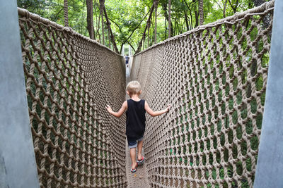 Full length of boy walking on footbridge in forest