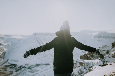 Back view of anonymous female traveler standing with outstretched arms and enjoying freedom in highlands in winter in svalbard
