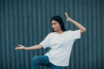 Young woman looking away while standing against wall