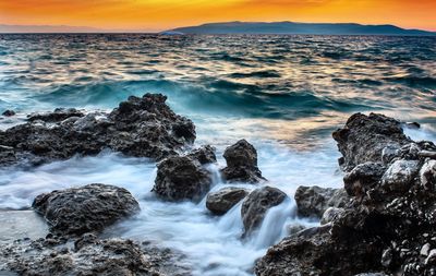 Rocks in sea against sky during sunset