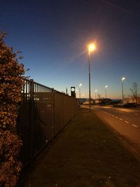 Street amidst illuminated road against clear sky during sunset