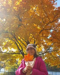 Portrait of young woman standing by tree during autumn