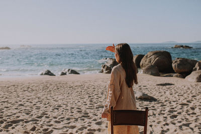 Rear view of woman sitting on beach against clear sky