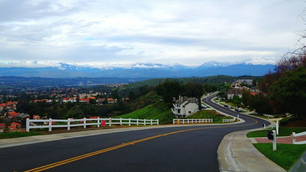 mountain, road, sky, the way forward, road marking, transportation, mountain range, cloud - sky, building exterior, street, built structure, cloud, architecture, tree, landscape, country road, cloudy, nature, high angle view, outdoors