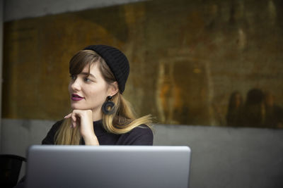 Smiling businesswoman with hand on chin by laptop in office