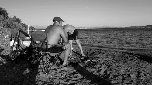 Man sitting on shore at beach against sky