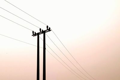 Low angle view of silhouette electricity pylon against clear sky