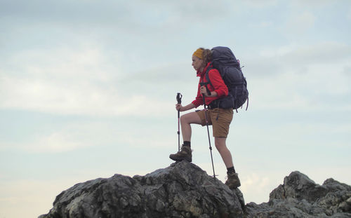 Full length side view of woman holding hiking poles standing on rocks