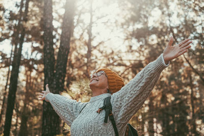 Rear view of woman with arms outstretched standing in forest