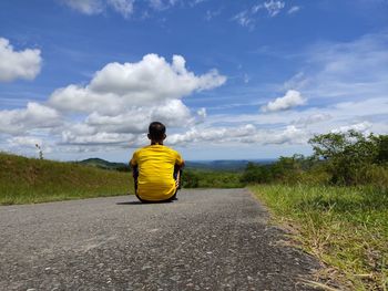 Rear view of man sitting on road against sky