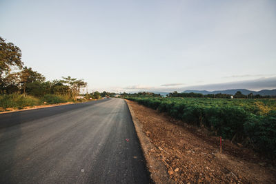 Empty road amidst field against sky