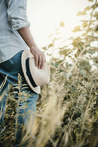 Midsection of man holding hat while standing on field