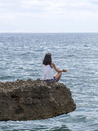 Rear view of woman meditation on rock against sea