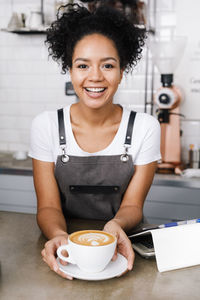 Portrait of barista holding coffee cup at cafe