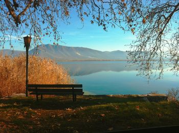 Empty bench by lake against sky